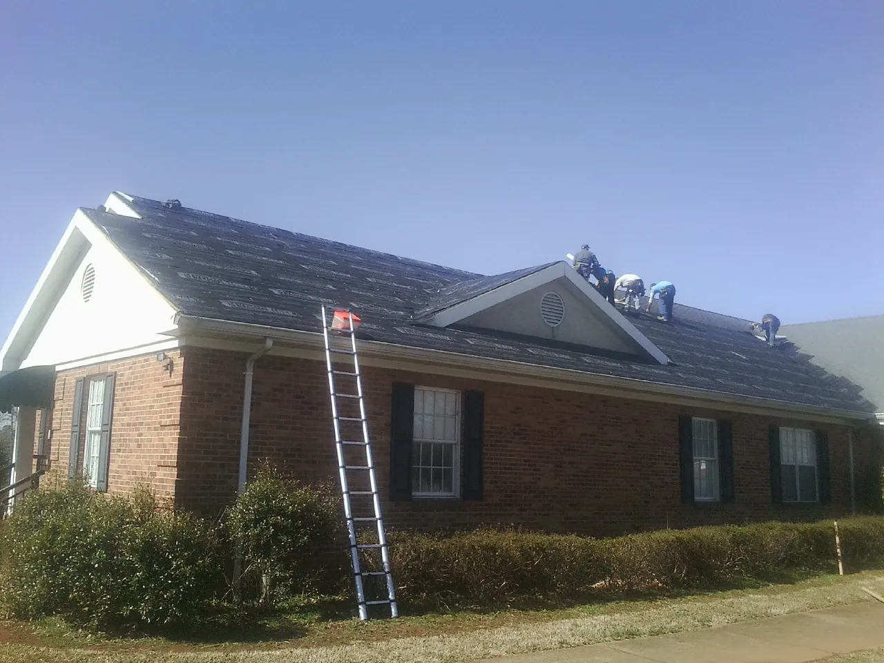 Crew tearing shingles off a brick ranch roof with a ladder set — Metal Roof Repair work by our crew in Brownsville